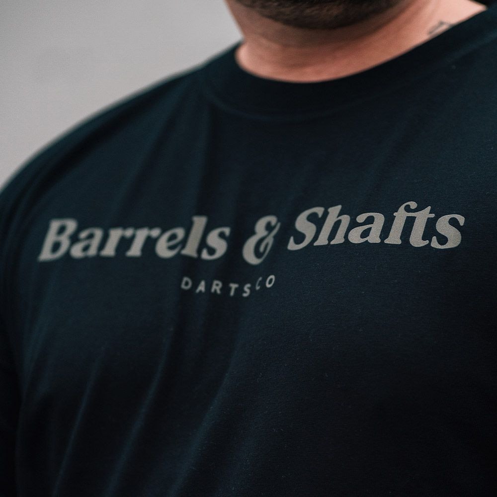Barrels and Shafts T-Shirt - Schwarz Das Bild zeigt ein schwarzes T-Shirt mit der Aufschrift "Barrels & Shafts". Darunter steht in kleineren Buchstaben "DARTSCO".
