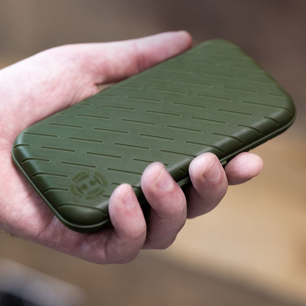 Harrows Slimcase Darttasche Eine Hand hält ein schlankes, grünes Etui. Das Etui hat ein strukturiertes Muster und ein rundes Logo in der Ecke.