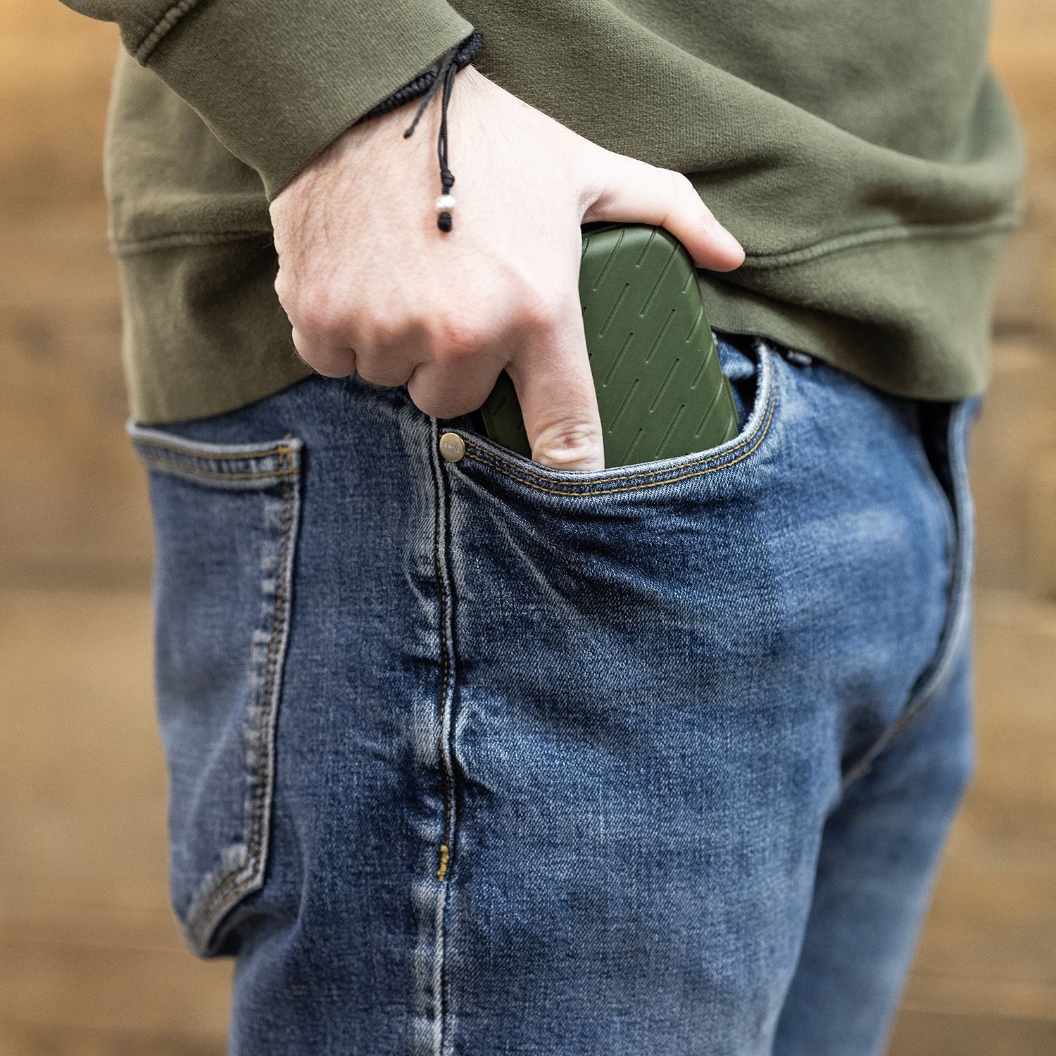 Harrows Slimcase Darttasche Eine Person steckt ein grünes Etui in die vordere Hosentasche einer Jeans. Das Etui hat eine strukturierte Oberfläche und passt gut in die Tasche.