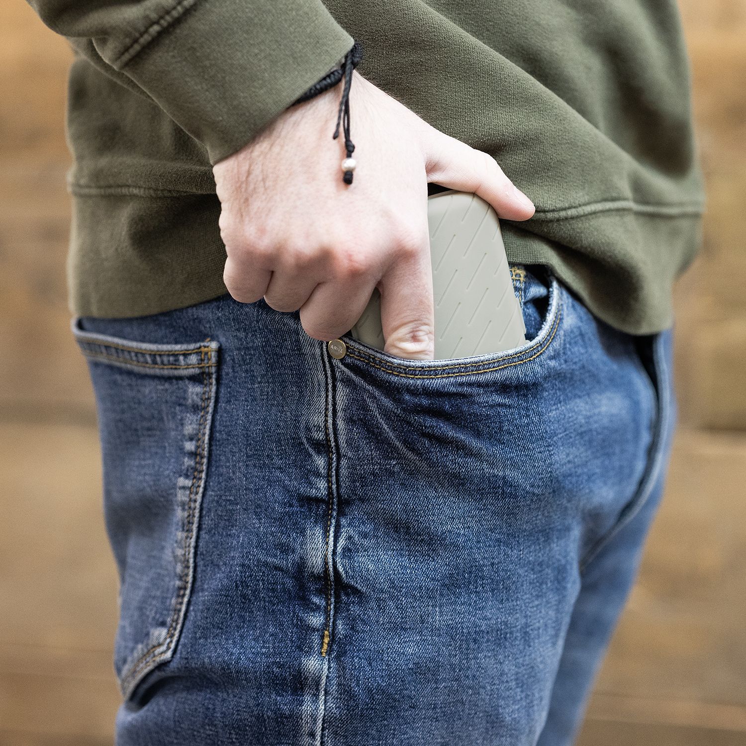 Harrows Slimcase Darttasche Eine Person steckt eine graue Darttasche in ihre Hosentasche. Die Person trägt eine blaue Jeans und einen olivgrünen Pullover.