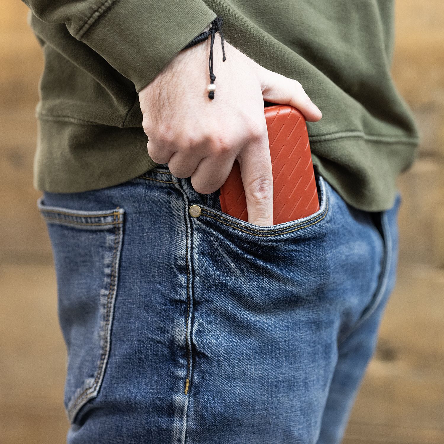 Harrows Slimcase Darttasche Eine Person steckt ein rotes Etui in die Hosentasche. Sie trägt eine blaue Jeans und einen grünen Pullover.